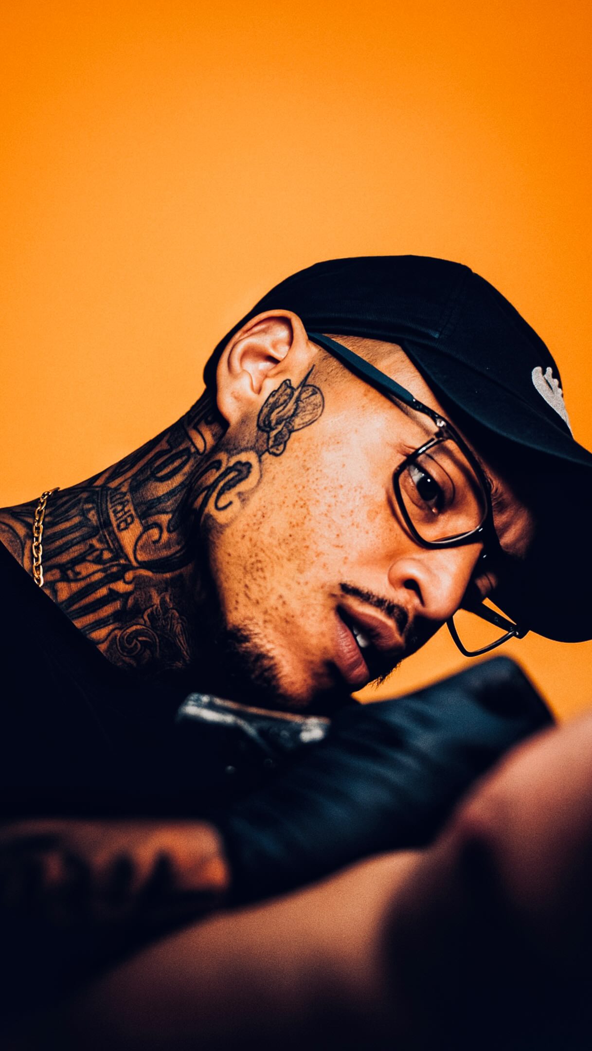 Wesley, tatuador, de boné e óculos em retrato com fundo laranja